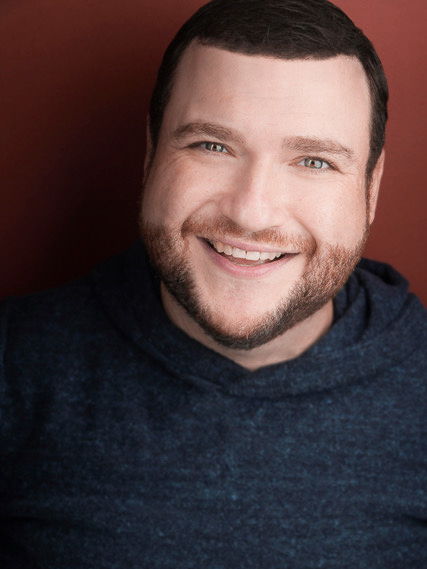Buonopane Todd – The REV Theatre Co. | Broadway in the Finger Lakes Smiling man with short dark hair and beard in a navy hoodie, against a warm brown background.