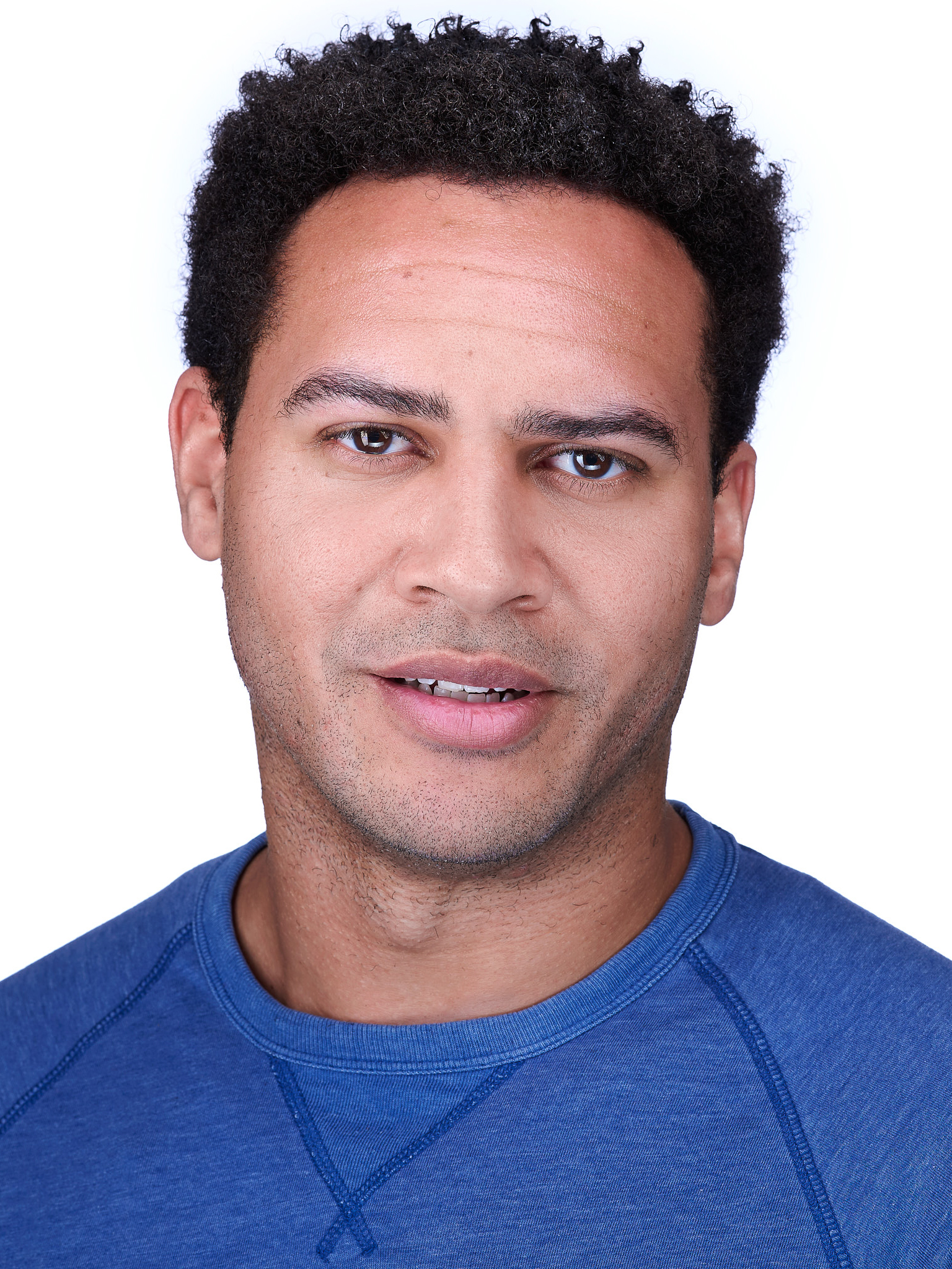 Cole Cordell – The REV Theatre Co. | Broadway in the Finger Lakes Close-up portrait of a man with short curly black hair wearing a blue crewneck shirt, facing forward.